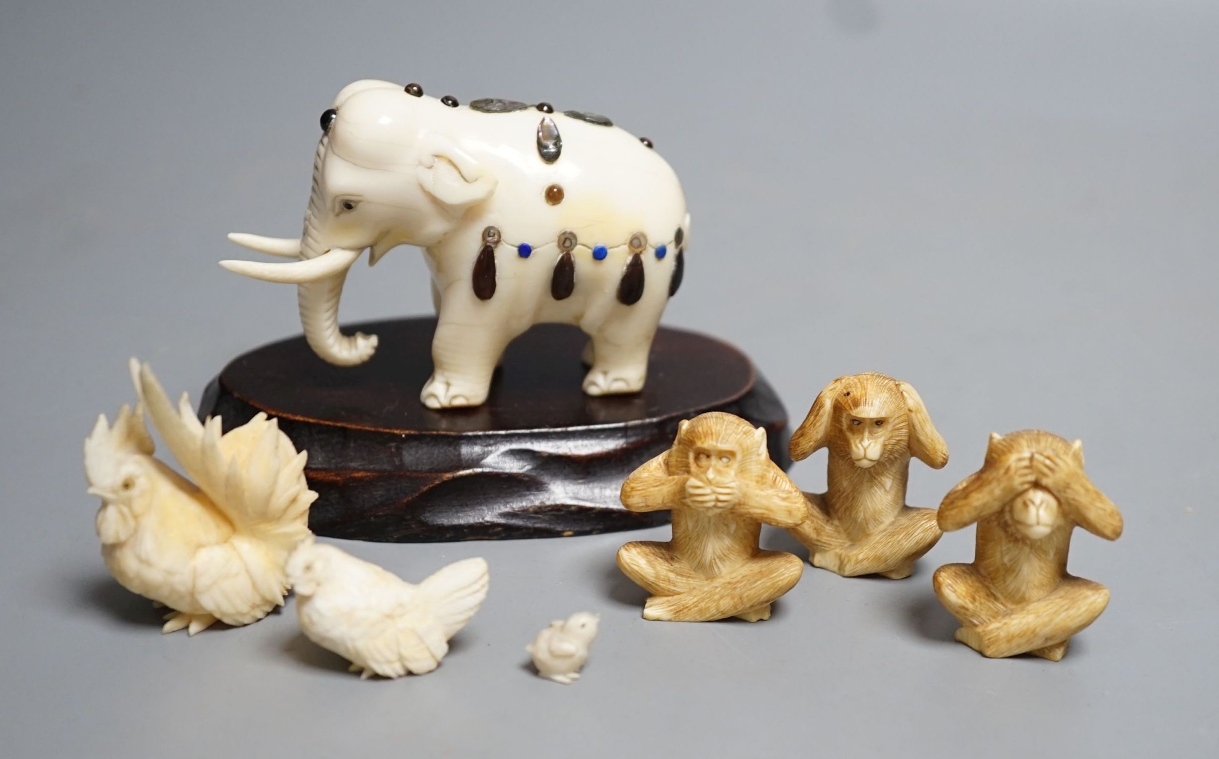 A Japanese Ivory and Shibayama style model of an elephant, three Japanese Ivory figures of the three wise monkeys and three Japanese ivory models of chickens and a chick, wood stand, all late 19th/early 20th century